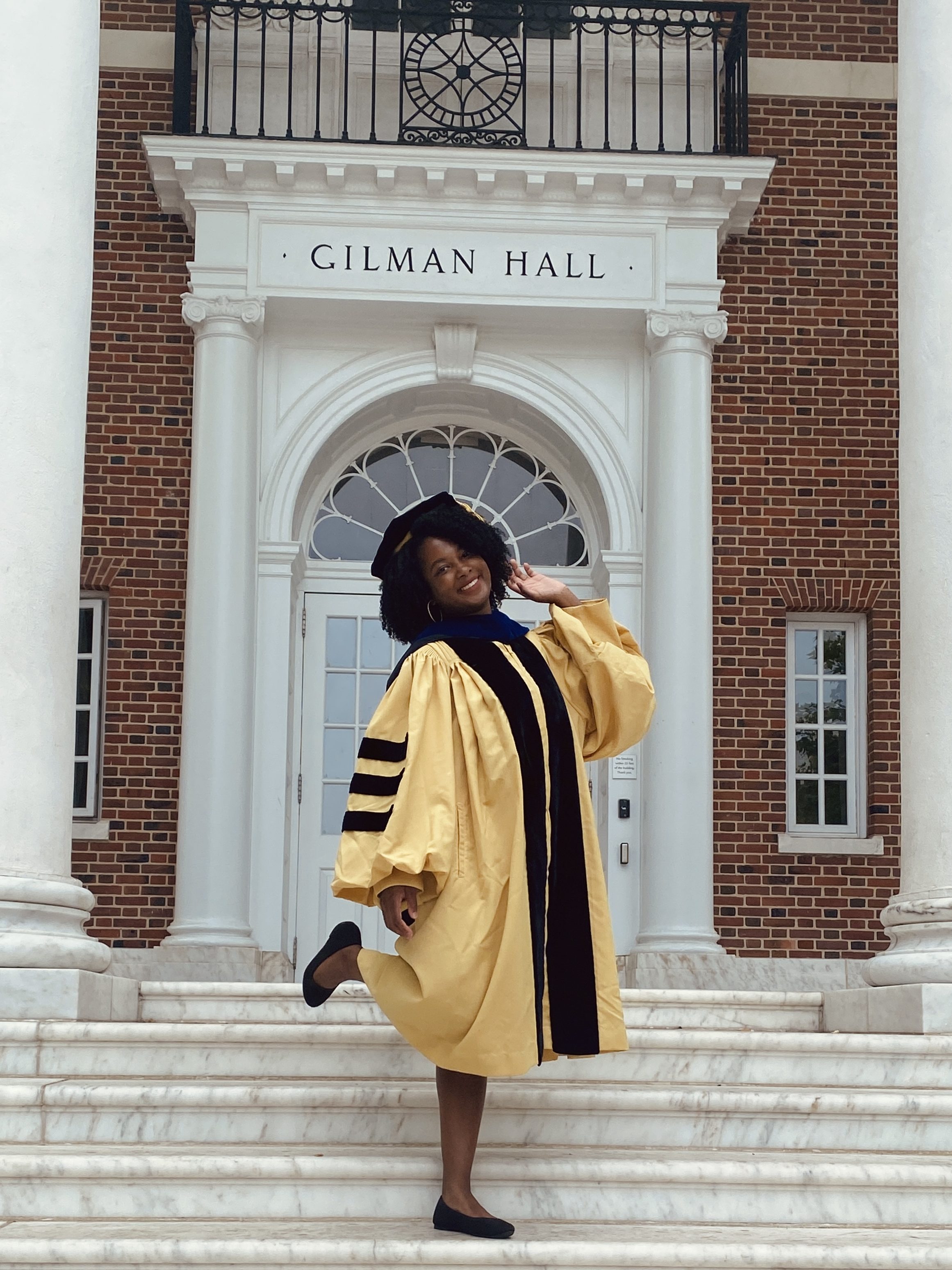 Graduation photo on the steps of Gilman Hall at Johns Hopkins University. Pictured graduated is wearing a yellow and black Ph.D. graduation robe.